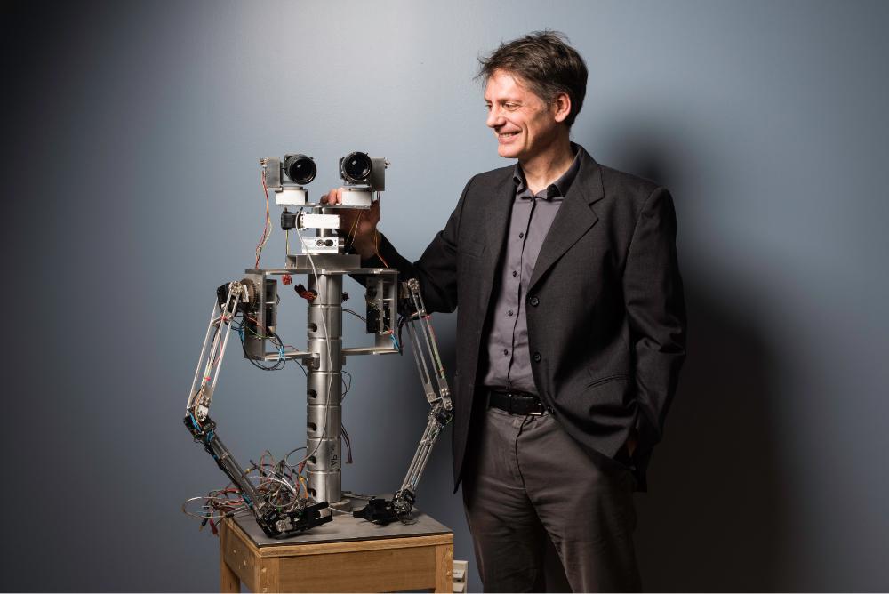 Faculty robotics researcher standing next to robot head and upper torso at University of Rochester