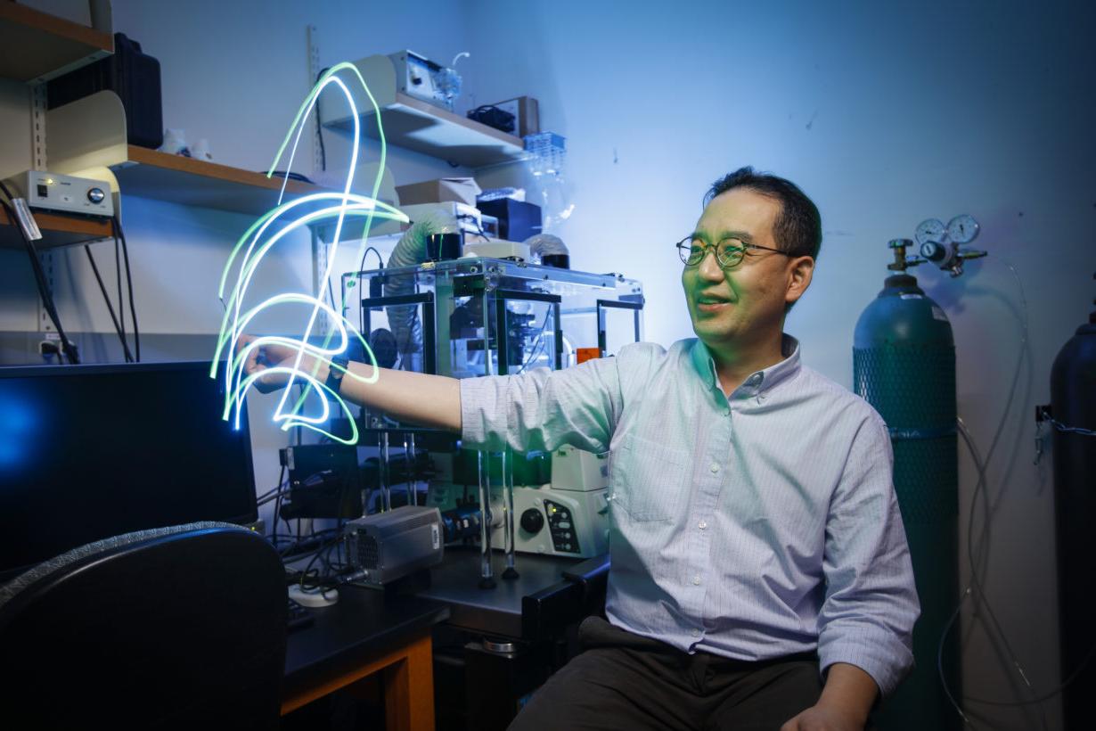 University of Rochester employee in lab moving pieces of fiber optic cable emitting streaks of blue and green light