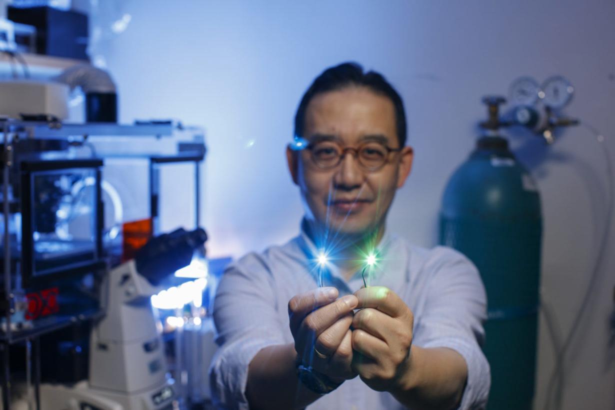 University of Rochester employee in lab holding pieces of fiber optic cable emitting blue and green light from the ends