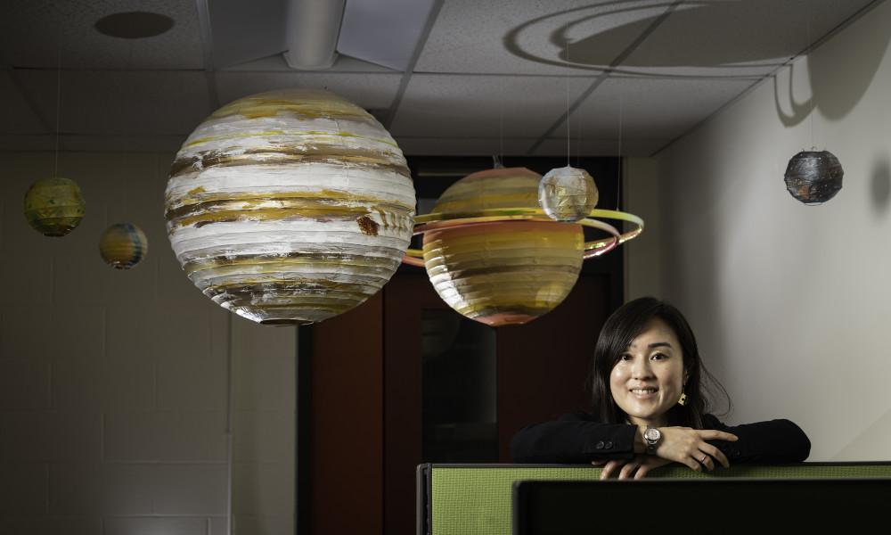 Woman surrounded by hanging model planets to illustrate moon formations.