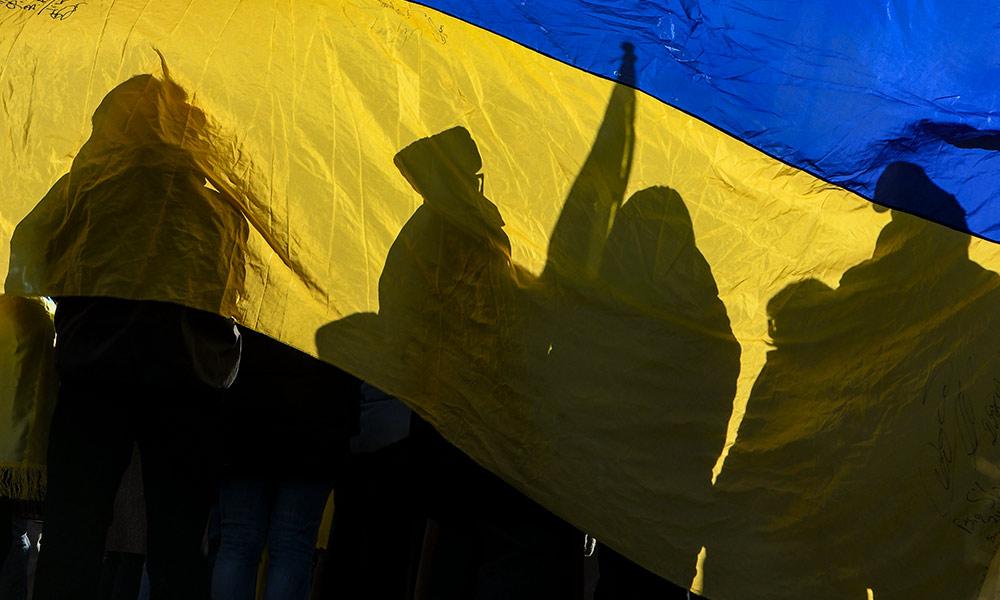 protesters holding signs, viewed through a Ukrainian flag.