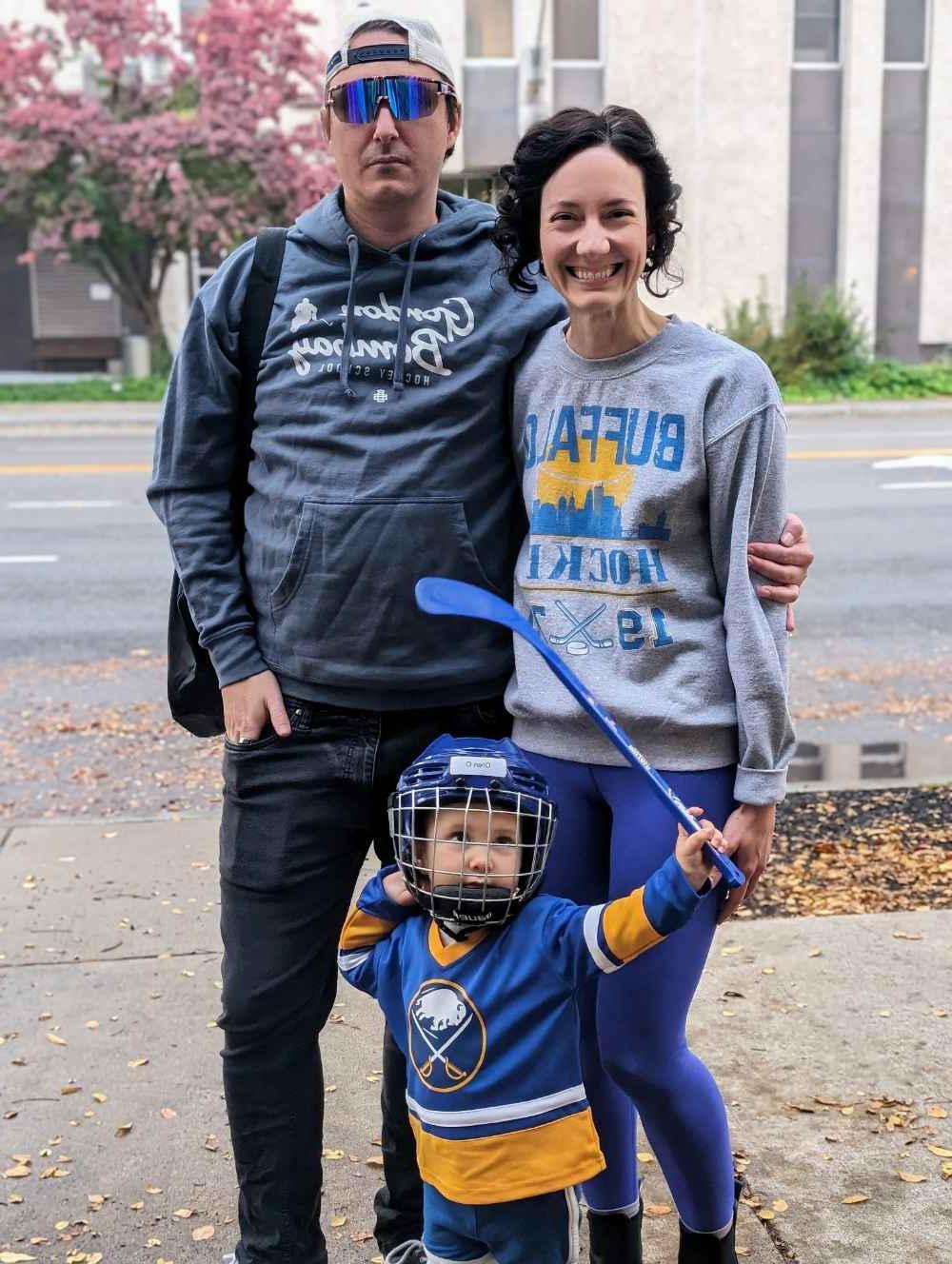Mitch O'Connell with his partner pose with their two-year-old, who is sporting ice hockey gear.