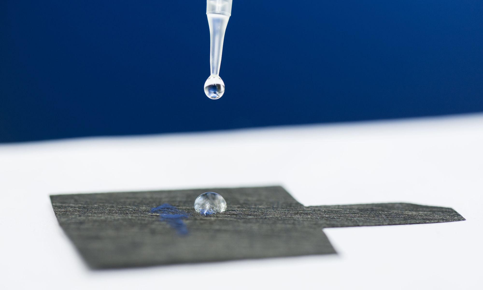 Pipette releasing a water droplet atop carbon paper to illustrate pfas chemical remediation.